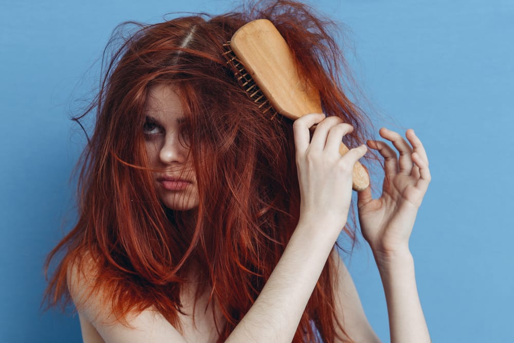 Woman brushing tangled red hair.