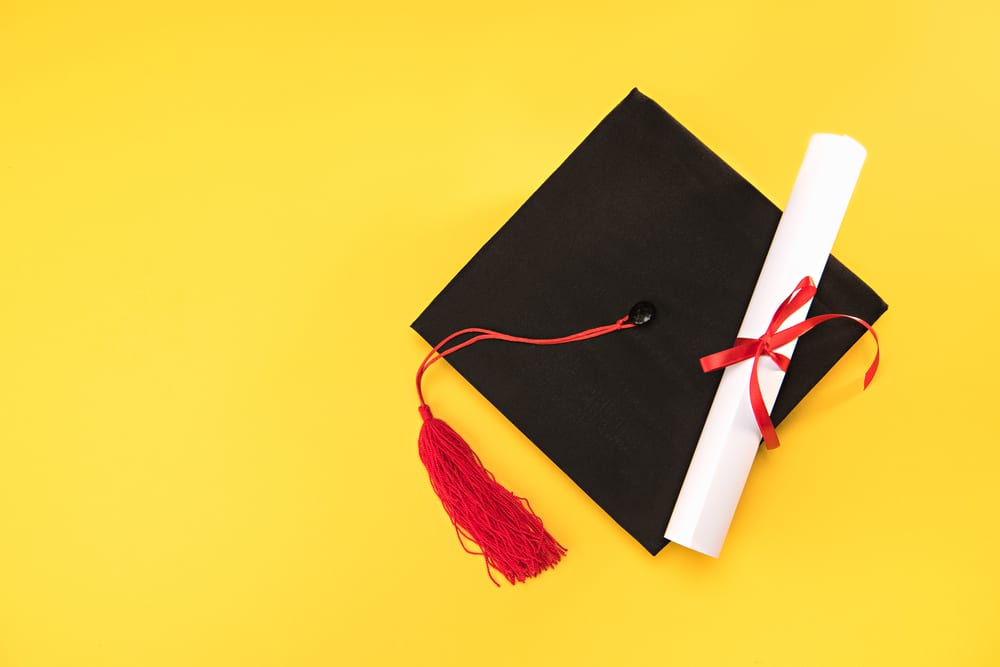 Graduation cap with a diploma on a yellow background.