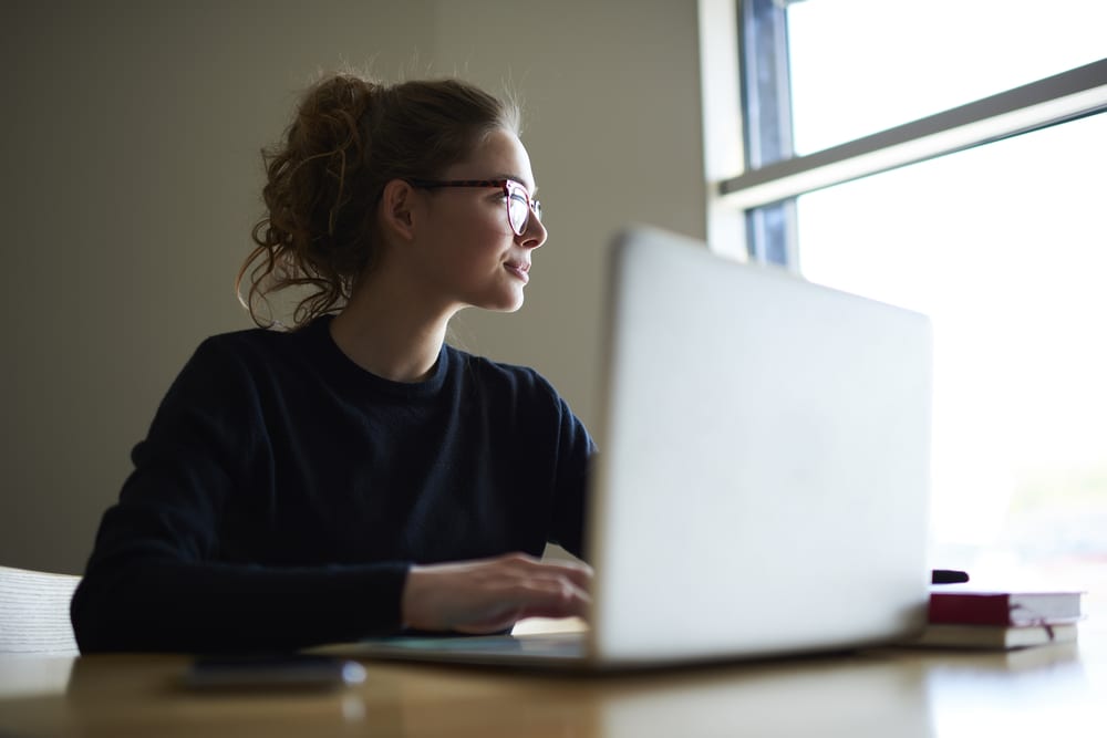 Girl in a black sweater wearing glasses sits at a laptop.